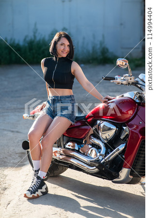 Brunette woman in shorts on a red motorcycle. Brunette woman in shorts on a red motorcycle. 114994404