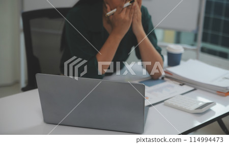 Asian women sitting in a home office With stress and eye strain.Tired businesswoman holding eyeglasses and massaging nose bridge. There are tablets, laptops, and coffee. Asian women sitting in a home office With stress and eye strain.Tired businesswoman holding eyeglasses and massaging nose bridge. There are tablets, laptops, and coffee. 114994473