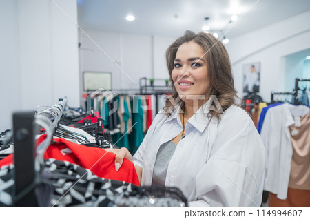 A fat woman looks with horror at the price tag on a dress in a plus size store.  114994607