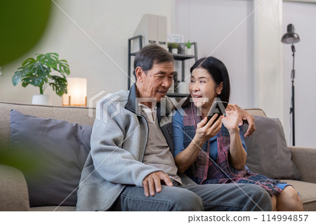 Senior couple enjoying time at home with smartphone. Concept of technology, companionship, and relaxation 114994857