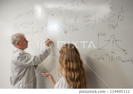An elderly man and a young woman at a white board. Colleagues scientists discuss work issues. An elderly man and a young woman at a white board. Colleagues scientists discuss work issues. 114995112