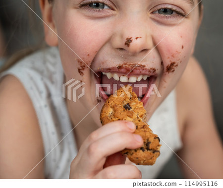 A cute little girl smeared in chocolate eats cookies while lying on the sofa. A cute little girl smeared in chocolate eats cookies while lying on the sofa. 114995116