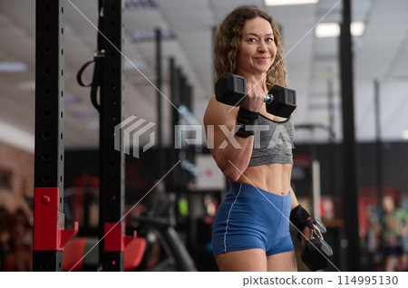 Muscular Caucasian forty year old woman doing exercises with dumbbells in the gym.  114995130