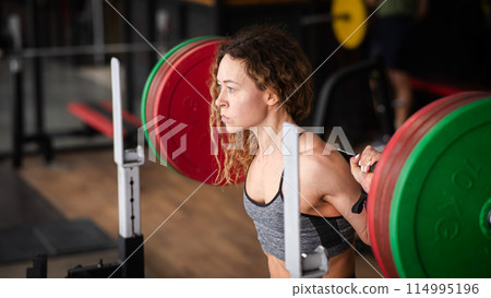 Middle-aged woman doing squats with a barbell in the gym. Middle-aged woman doing squats with a barbell in the gym. 114995196