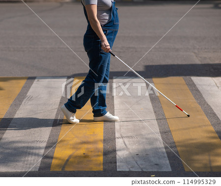 Close-up of the legs of a blind woman crossing the road at a crosswalk with a cane. Close-up of the legs of a blind woman crossing the road at a crosswalk with a cane. 114995329