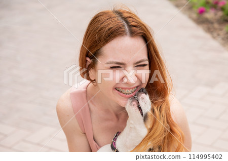 Dog jack russell terrier licks the owner in the face outdoors. Girl with braces on her teeth. Dog jack russell terrier licks the owner in the face outdoors. Girl with braces on her teeth. 114995402