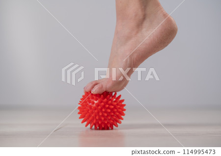 Close-up of a woman's foot on a massage ball with spikes.  114995473