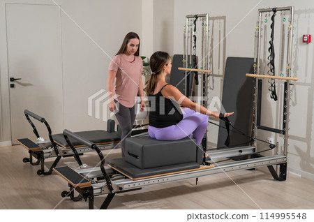 Caucasian pregnant woman doing Pilates exercises on a reformer machine with an individual trainer. Caucasian pregnant woman doing Pilates exercises on a reformer machine with an individual trainer. 114995548