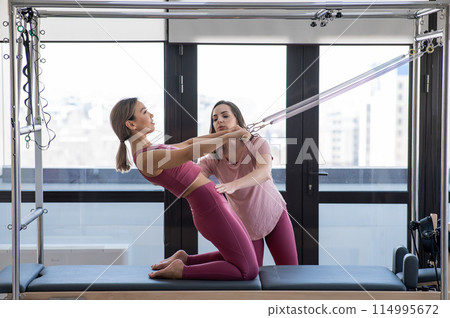 Asian woman doing pilates with trainer on cadillac reformer.  Asian woman doing pilates with trainer on cadillac reformer.  114995672