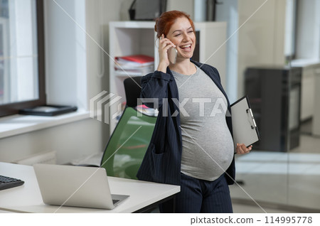Pregnant woman using mobile phone and holding paper tablet in office.  114995778