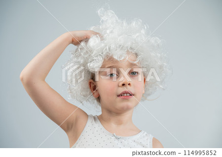Portrait of a little Caucasian girl wearing a white curly wig on a white background.  114995852