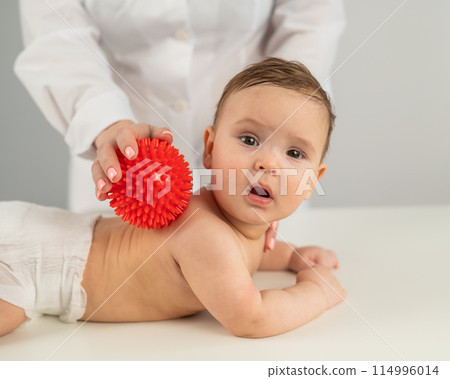 A doctor gives a child a back massage using a ball. 114996014