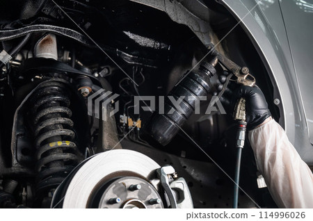 An auto mechanic applies anti-corrosion mastic to the underbody of a car. An auto mechanic applies anti-corrosion mastic to the underbody of a car. 114996026