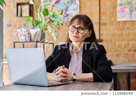 Middle-aged business woman working remotely with laptop in coworking Middle-aged business woman working remotely with laptop in coworking 114996049