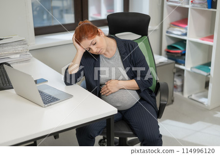 Pregnant woman sleeping at her desk in the office. Pregnant woman sleeping at her desk in the office. 114996120