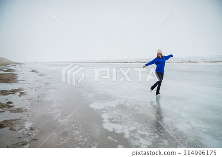 Caucasian woman in a blue sweater is skating on a frozen lake. The figure skater performs the program. Caucasian woman in a blue sweater is skating on a frozen lake. The figure skater performs the program. 114996175