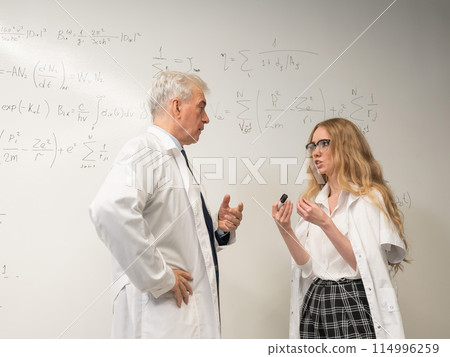 An elderly man and a young woman at a white board. Colleagues scientists discuss work issues.  114996259