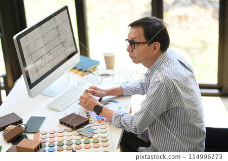 Experienced senior interior designer in eyeglasses working on new project at creative office Experienced senior interior designer in eyeglasses working on new project at creative office 114996273