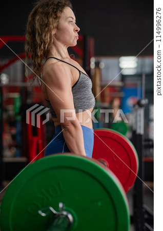 Middle aged woman doing deadlifts in the gym. Vertical photo. Middle aged woman doing deadlifts in the gym. Vertical photo. 114996276