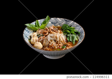A bowl of Spicy Thai noodles soup with pork offal, meatballs and vegetables on black background 114996311