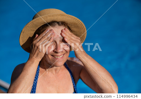 Portrait of an older woman applying sunscreen to her face while on vacation.  114996434