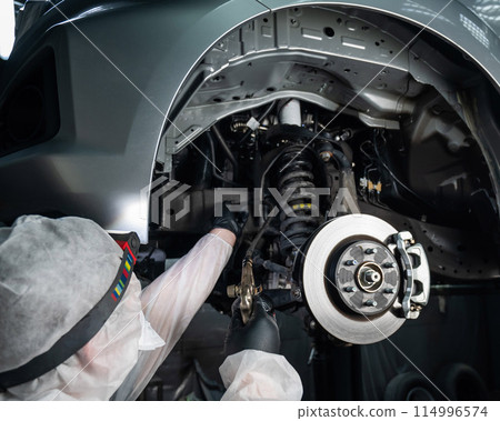 An auto mechanic applies anti-corrosion mastic to the underbody of a car. An auto mechanic applies anti-corrosion mastic to the underbody of a car. 114996574