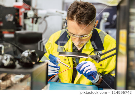 Electrician technician caucasian male using hot soldering iron to electrical bond electricity wire fix repair power line cable with solder tin and lead. Electrician technician caucasian male using hot soldering iron to electrical bond electricity wire fix repair power line cable with solder tin and lead. 114996742