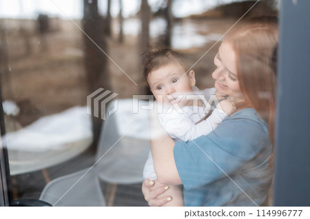 View through the window of a red-haired Caucasian woman holding her little son. View through the window of a red-haired Caucasian woman holding her little son. 114996777