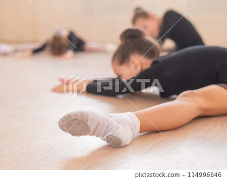 Girls ballerinas stretch while lying in a wide fold.  114996846