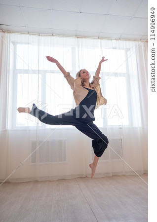 Caucasian woman dances contemporary in ballet class. Dancer in a jump. Vertical photo. Caucasian woman dances contemporary in ballet class. Dancer in a jump. Vertical photo. 114996949