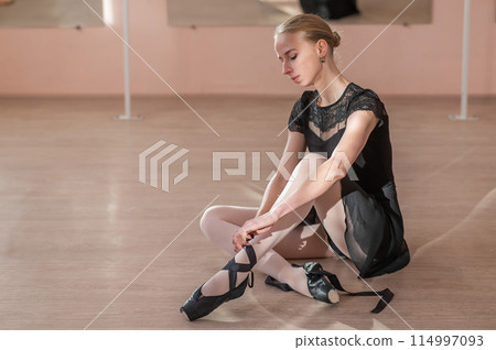 Woman sitting on the floor and tying ribbons on her pointe shoes. Woman sitting on the floor and tying ribbons on her pointe shoes. 114997093