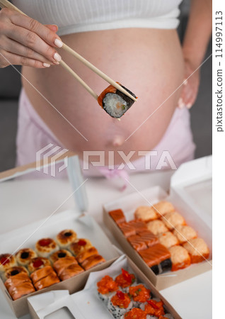 A pregnant woman stands at a table with rolls. Close-up of the belly. A pregnant woman stands at a table with rolls. Close-up of the belly. 114997113