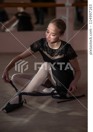 Woman sitting on the floor and tying ribbons on her pointe shoes. Vertical photo. Woman sitting on the floor and tying ribbons on her pointe shoes. Vertical photo. 114997163