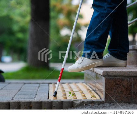 Close-up of female foot, walking stick and tactile tiles. Blind woman walking down stairs using a cane. Close-up of female foot, walking stick and tactile tiles. Blind woman walking down stairs using a cane. 114997166