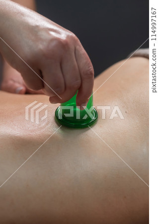 A woman undergoes an anti-cellulite massage procedure using a vacuum jar. Close-up of the lower back. Vertical photo. A woman undergoes an anti-cellulite massage procedure using a vacuum jar. Close-up of the lower back. Vertical photo. 114997167