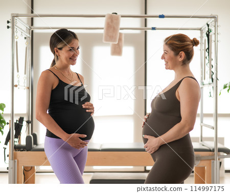 Two pregnant women communicate in a fitness club. Pilates for expectant mothers. Two pregnant women communicate in a fitness club. Pilates for expectant mothers. 114997175