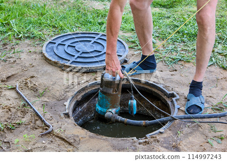 Worker pumps sewage out of septic tank using submersible drainwater pump. 114997243