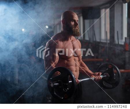 Caucasian bald topless man doing an exercise with a barbell in the gym. Bicep curls with weights. 114997248