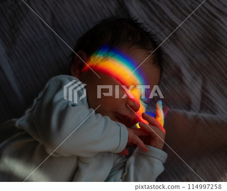 Close-up portrait of a newborn boy with a prism beam on his face. Rainbow. Close-up portrait of a newborn boy with a prism beam on his face. Rainbow. 114997258
