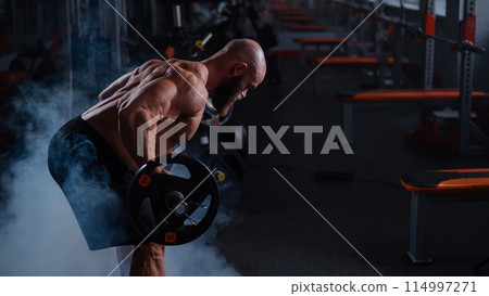 Caucasian bald topless man doing an exercise with a barbell in the gym.  114997271