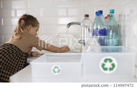 Against the background of boxes with a recycling sign, a child sorts plastic. A small child helps put plastic bottles into boxes for recycling. Concept of sorting plastic for recycling. Against the background of boxes with a recycling sign, a child sorts plastic. A small child helps put plastic bottles into boxes for recycling. Concept of sorting plastic for recycling. 114997472