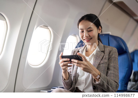 Smiling businesswoman using smartphone on airplane. Concept of in flight communication and business travel Smiling businesswoman using smartphone on airplane. Concept of in flight communication and business travel 114998677
