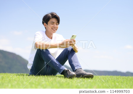 man looking at smartphone on lawn 114999703