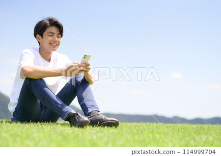 man looking at smartphone on lawn 114999704