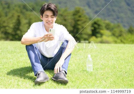 男人在草坪上看智能手機 114999719