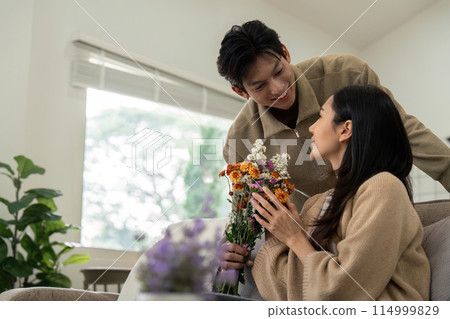 Young couple sharing a bouquet at home. Concept of love, affection, and togetherness Young couple sharing a bouquet at home. Concept of love, affection, and togetherness 114999829