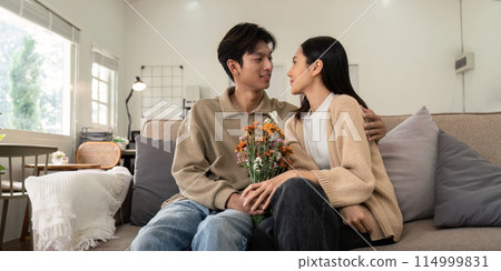 Young couple sitting together with flowers at home. Concept of love, affection, and intimacy Young couple sitting together with flowers at home. Concept of love, affection, and intimacy 114999831