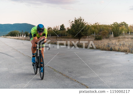 Triathlete riding his bicycle during sunset, preparing for a marathon. The warm colors of the sky provide a beautiful backdrop for his determined and focused effort. 115000217