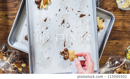 Flat lay. Carefully packaging Christmas cutout cookies, half-dipped in chocolate, sprinkled with crushed nuts, and presented in clear cellophane wrapping. 115000302