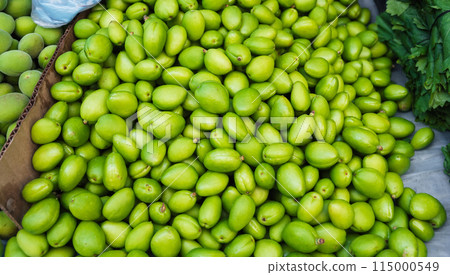 unripe green apricot on counter of a bazaar in Uzbekistan. Traditional Uzbek food on market shelf - green uryuk, dovcha, gura 115000549